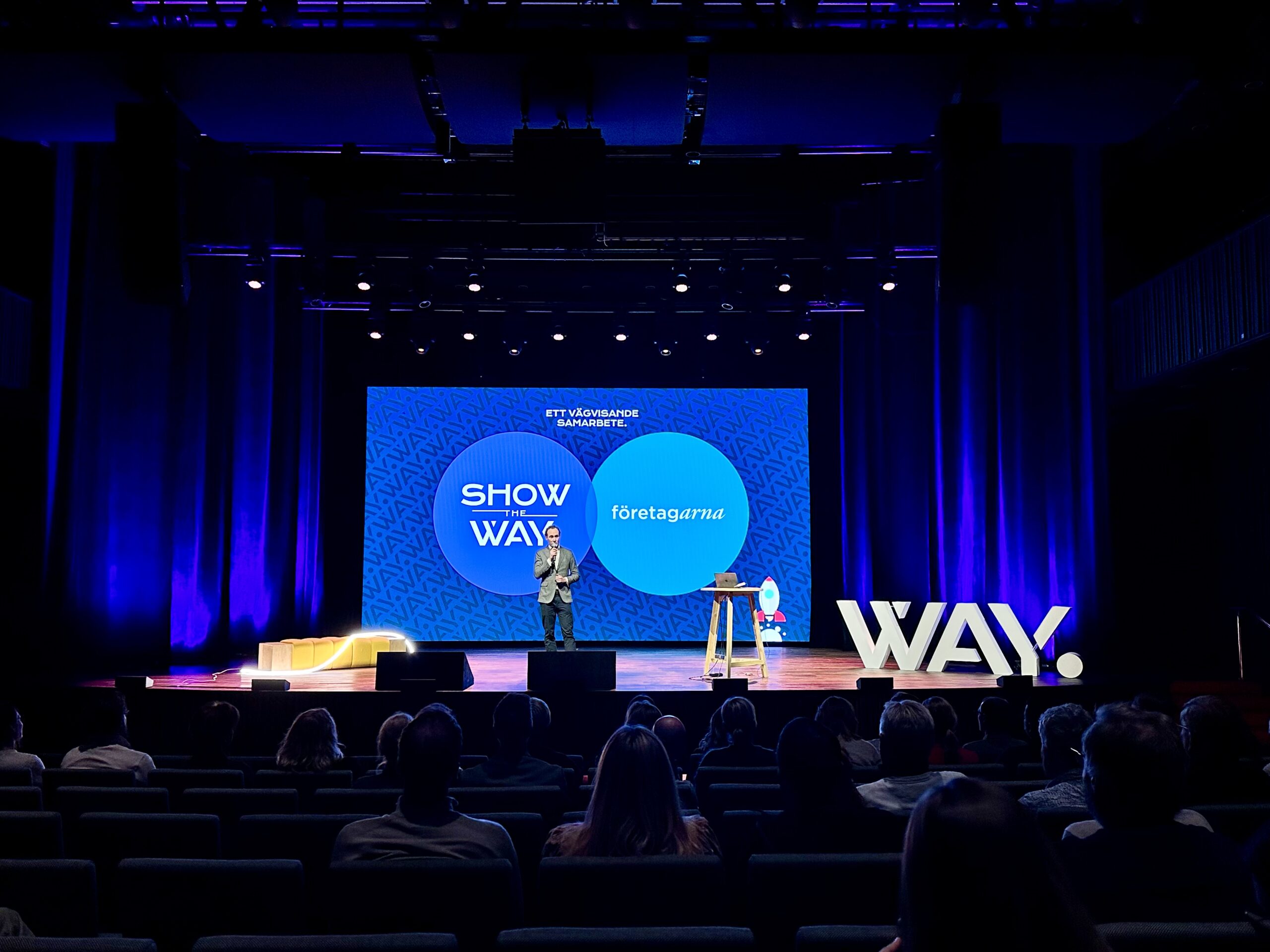 Alfred Appelros står på en stor scen och talar, med Way Communications logotyp i bakgrunden. En inspirerande presentation om framtidens marknadsföring.